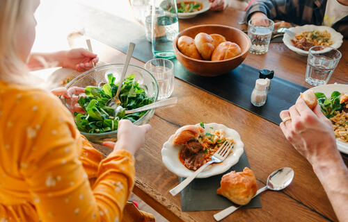 Familie mit Kindern sitzt am Esstisch und teilt Essen auf | © Land schafft Leben