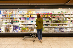 Blonde Frau steht mit halbvollem Wagerl vor Milchprodukten im Supermarkt | © Land schafft Leben